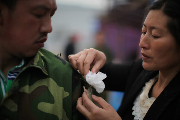 A woman pins a paper flower on her husband's sleeve on Saturday in Renjia village, Qingren township, in Sichuan province's Lushan county, to pay respect to those who died in the earthquake. Wang Jing / China Daily  Life goes on after tragedy